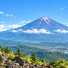 Mount Fuji rising above green foothills under a clear summer sky.