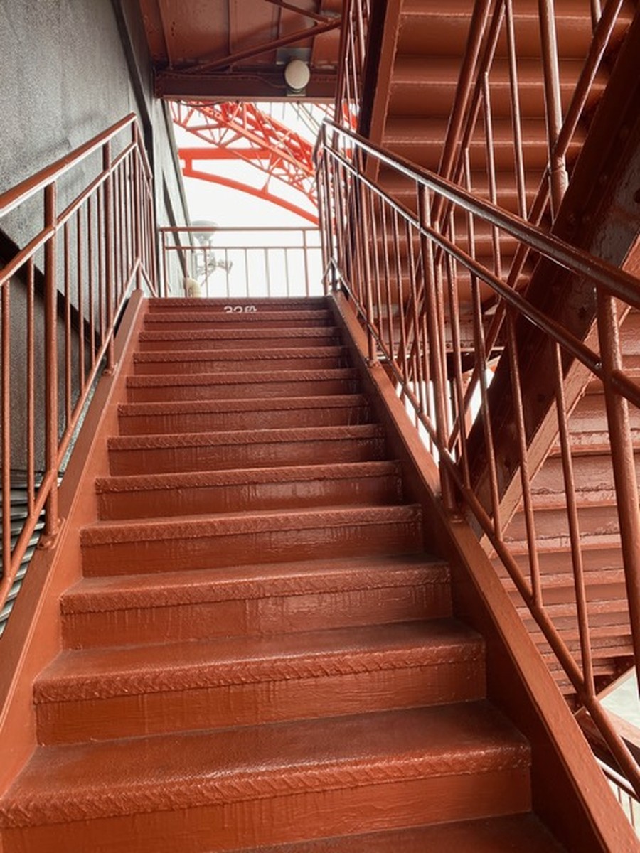 A straight flight of Tokyo Tower's outdoor stairs, with handrails on both sides and the tower's steel frame visible at the top.